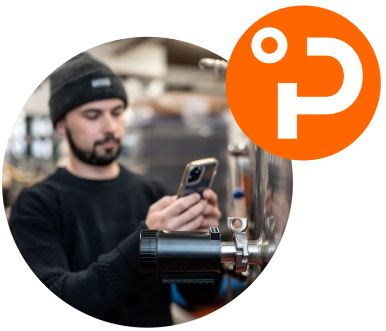 Mann überwacht Brauprozess mit PLAATO Sensor und Smartphone. Im Eck des Bildes hängt ein oranger Kreis mit weißem PLAATO-Signet