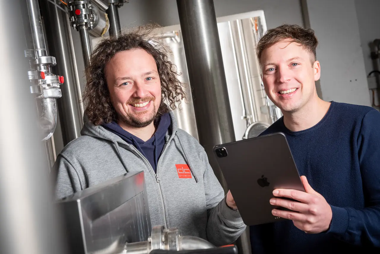 Andreas (left) and Michael (right) Weisenseel stand in a brewery with a tablet and check the system using MINGLECONTROL.